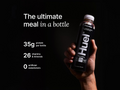 Hand holding a Huel protein shake bottle with product details on a black background