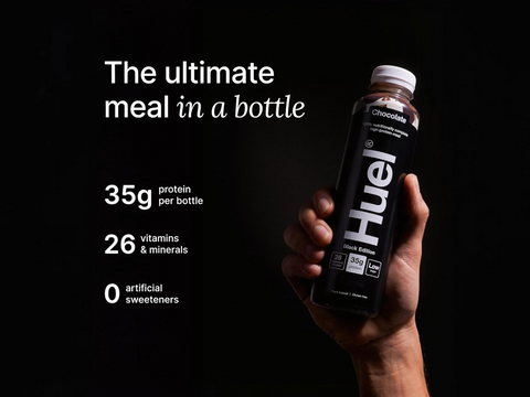 Hand holding a Huel protein shake bottle with product details on a black background