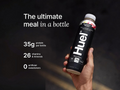 Hand holding a Huel protein shake bottle with nutritional information on a dark background