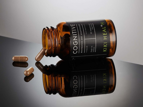Brown bottle labeled 'Cognitive' by Kiki Health with scattered capsules on a reflective surface.