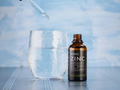 Bottle of KIKI Health Ionic Zinc supplement with a dropper and glass on a blue background