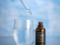 Bottle of oil with dropper and glass against a blurred blue background