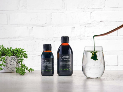 Two bottles of Niki Health Liquid Chlorophyll on a white surface with a glass of water and plant in the background.