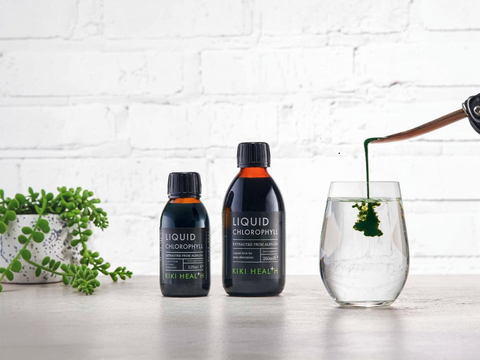 Two bottles of Niki Health Liquid Chlorophyll on a white surface with a glass of water and plant in the background.