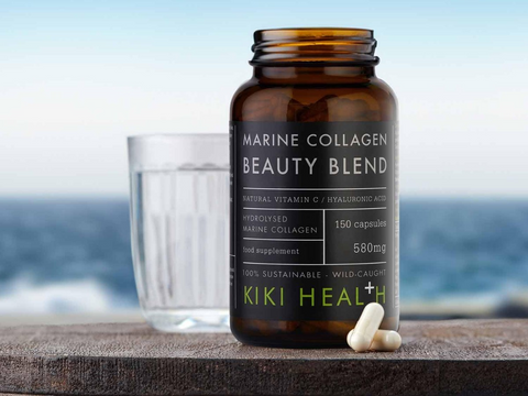 Kiki Health Marine Collagen Beauty Blend supplement bottle with a glass of water on a wooden surface with a blurred ocean background.