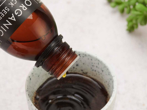 Bottle of organic oil being poured into a container on a light background