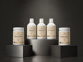 Five supplement containers from Organic Omega are arranged on dark display blocks against a dark gray studio background. Two white plastic bottles labeled Marine 15 and Marine 10 stand on a central pedestal, while two white jars labeled Bovine Pure and Marine Pure sit on lower blocks.