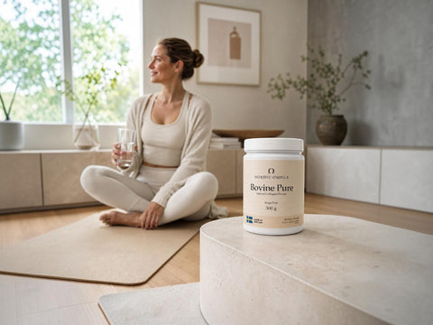 A woman in a cream workout outfit sits cross-legged on a yoga mat in a bright, modern room, holding a glass of water. In the foreground, a white tub of Bovine Pure supplement is displayed on a stone pedestal.