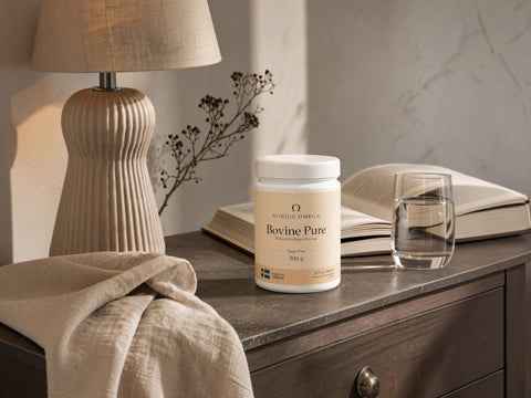 A white tub of Neuroline Chamomile 'Boxine Pure' herbal supplement sits on a dark wooden nightstand in a cozy, warmly lit bedroom setting, surrounded by a lamp, an open book, a glass of water, and a beige linen throw.