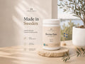 Nordic Omega Boveine Pure supplement tub displayed on a stone coaster on a wooden table, with a potted plant and a small Swedish flag in a bright, sunlit room.