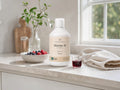 A bottle of Organic Omega Marine 10 liquid supplement sits on a light stone countertop in a bright kitchen setting, with a bowl of berries, a glass of dark liquid, and a folded towel nearby.