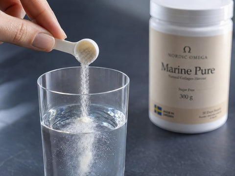 A hand holds a small white scoop pouring powder into a glass of water, with a white jar labeled Nordic Omega Marine Pure in the background on a dark surface.