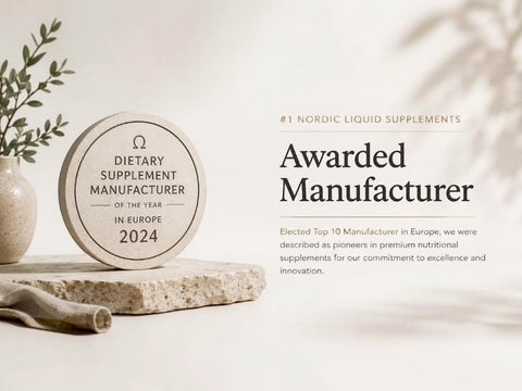 A round beige supplement award plaque reading 'Dietary Supplement Manufacturer of the Year in Europe 2024' sits on a stone slab beside a vase with greenery. Text on the right says '#1 Nordic Liquid Supplements' and 'Awarded Manufacturer' with additional descriptive copy.