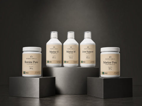 Five supplement containers from Organic Omega are arranged on dark display blocks against a dark gray studio background. Two white plastic bottles labeled Marine 15 and Marine 10 stand on a central pedestal, while two white jars labeled Bovine Pure and Marine Pure sit on lower blocks.