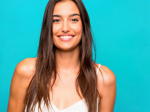 Woman with long brown hair smiling against a blue background