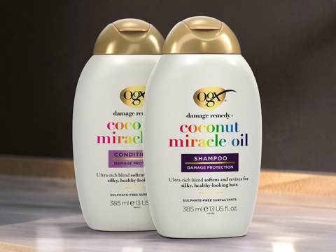 Two bottles of OGX Coconut Miracle Oil shampoo and conditioner on a wooden surface with a dark background.