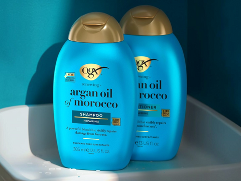 Two bottles of OGX shampoo and conditioner on a white surface with a blue background