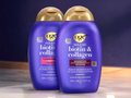 Two bottles of OGX thick & full biotin & collagen shampoo and conditioner on a wooden surface with a dark background.