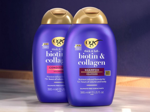 Two bottles of OGX thick & full biotin & collagen shampoo and conditioner on a wooden surface with a dark background.