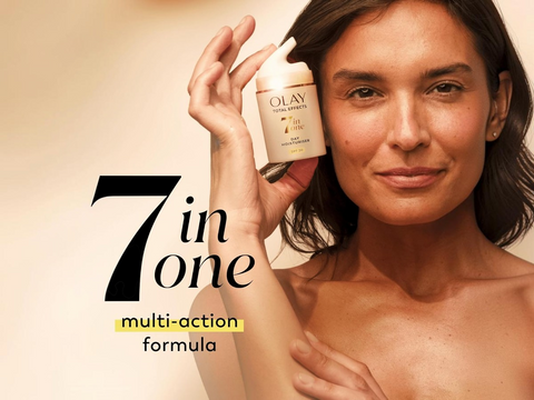 Woman holding an Olay skincare product with '7 in one' text on a beige background