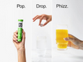 PHIZZ drink mix packaging with a hand holding a packet, a hand dropping it into a glass of orange juice, and the glass of juice being held.
