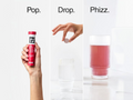 Hand holding a red bottle labeled 'PHIZZ', a pill being dropped into a glass of pink liquid, with text 'Pop.', 'Drop.