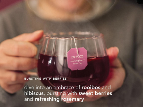 Person holding a glass of red drink with a Pukka tea bag, text about rooibos and hibiscus.