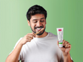 Man brushing his teeth with a toothbrush and holding a tube of toothpaste against a green background
