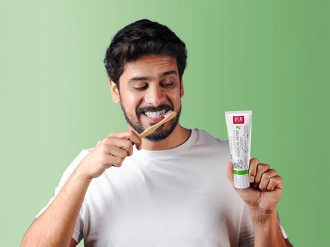 Man brushing his teeth with a toothbrush and holding a tube of toothpaste against a green background