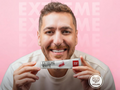 Man holding a tube of Extreme White toothpaste against a pink background