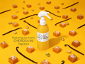Yellow bottle with white pump on a yellow background with vanilla beans and caramel pieces.