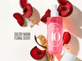 Pink bottle with white label surrounded by red fruits and flowers on a light background