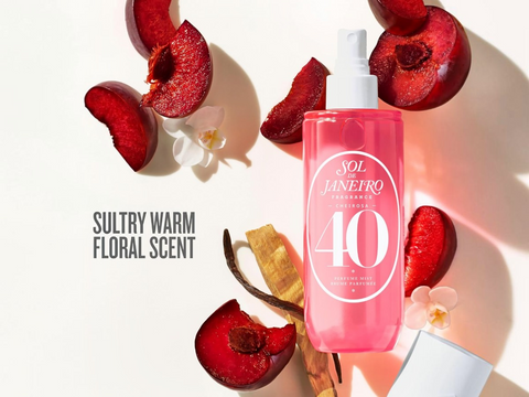Pink bottle with white label surrounded by red fruits and flowers on a light background