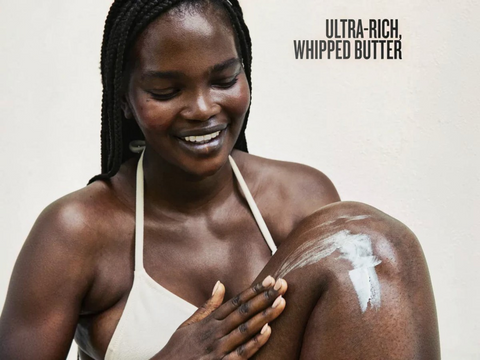 Woman applying ultra-rich whipped butter to her arm with a neutral background