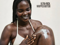 Woman applying ultra-rich whipped butter to her arm with a neutral background