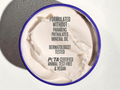 Container of cream with text about product ingredients and certifications on a gray background