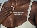 Person wearing a beige tank top with text 'Transfer-Resistant Barely-There Feel' on a close-up of skin.