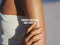 Close-up of a person's arm with text 'Transfer-Resistant Barely-There Feel' on a blurred background
