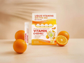 Box of Vitamin C+D3+K2 supplement with liquid vitamin bottle and oranges on a beige background