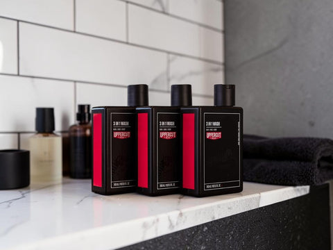 Three black rectangular bottles with red side panels and black caps, labeled 2-in-1 Hair, Skin, and Nails Treatment, arranged on a white marble countertop in a bathroom setting.