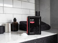 A bottle of Uppercut 3 in 1 Wash grooming product standing on a bathroom counter, with a white subway tile backsplash behind it and folded towels nearby.