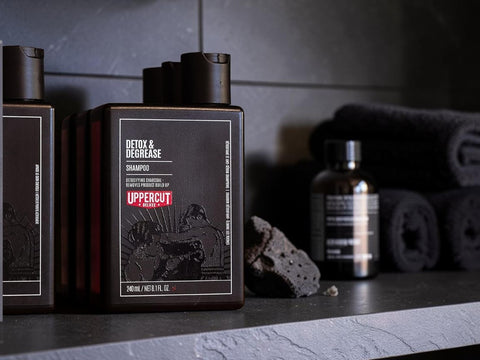 Uppercut Men Detox & Decrease Shampoo bottle on a dark stone surface with a towel and grooming stone in the background.