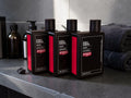 Three Uppercut Detox & Detangle shampoo bottles arranged on a dark countertop, with folded towels and bathroom accessories in the background.