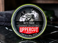 A round tin of Uppercut Barbers Collection Matte Pomade, featuring a black and white barber illustration with a red 'UPPERCUT' logo, set on a dark marble surface.