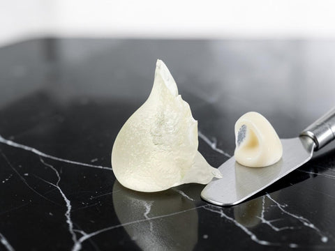 A translucent off-white silicone ear plug shown on a metal spatula against a black marble surface.