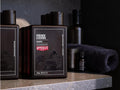 A dark brown rectangular bottle of Uppercut & Regain Shampoo on a stone countertop, with a matching towel and other grooming products blurred in the background.