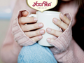 Person holding a white mug with Yogi Tea logo above