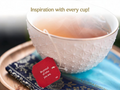 Teacup with a tea bag and a motivational tag on a blue cloth, with text 'Inspiration with every cup!'.