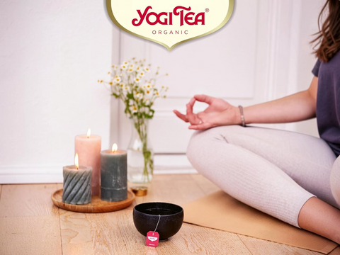 Person meditating with Yogi Tea products on a wooden floor